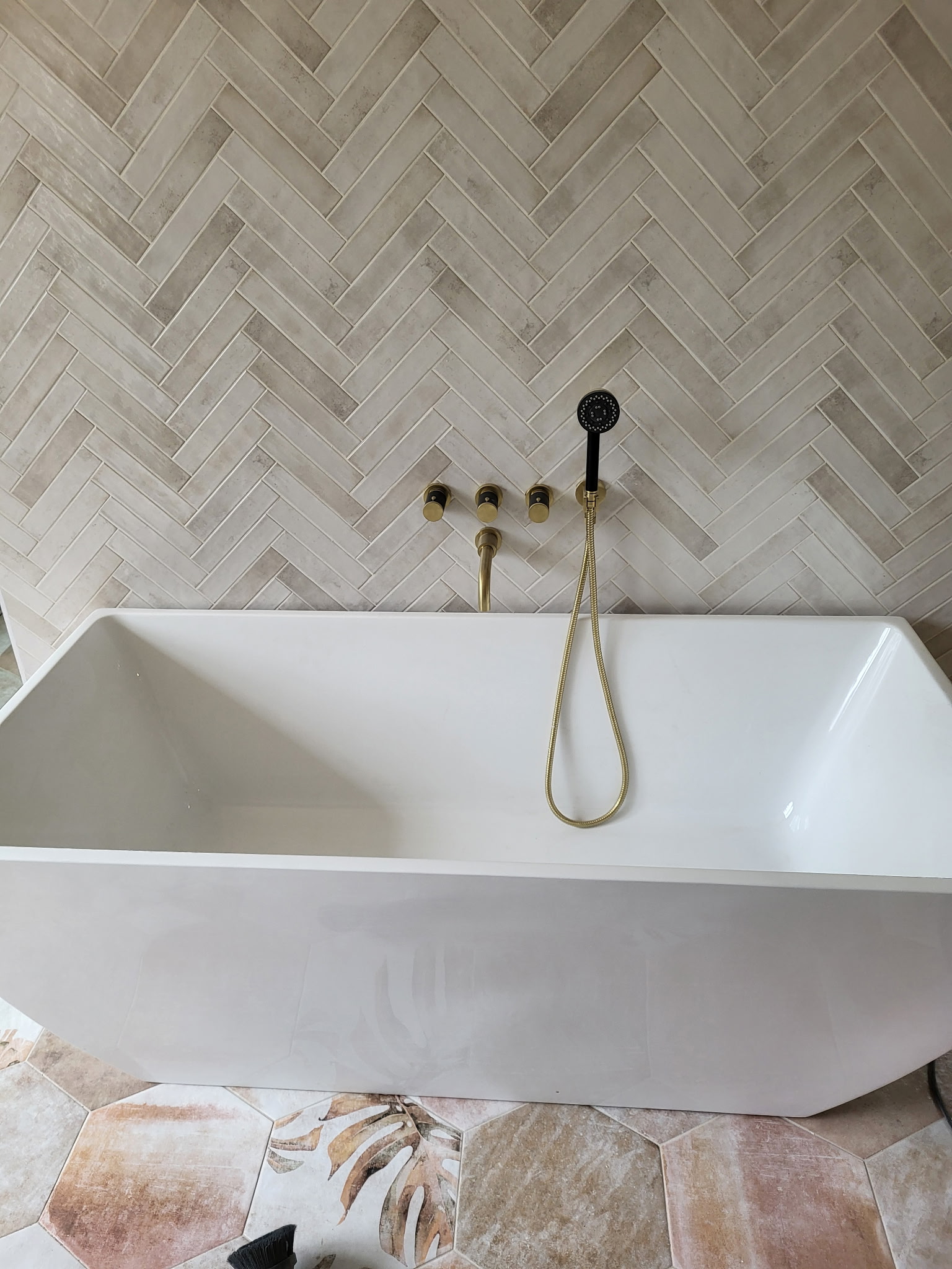 Freestanding soaker tub with herringbone tile and brushed gold fixtures
